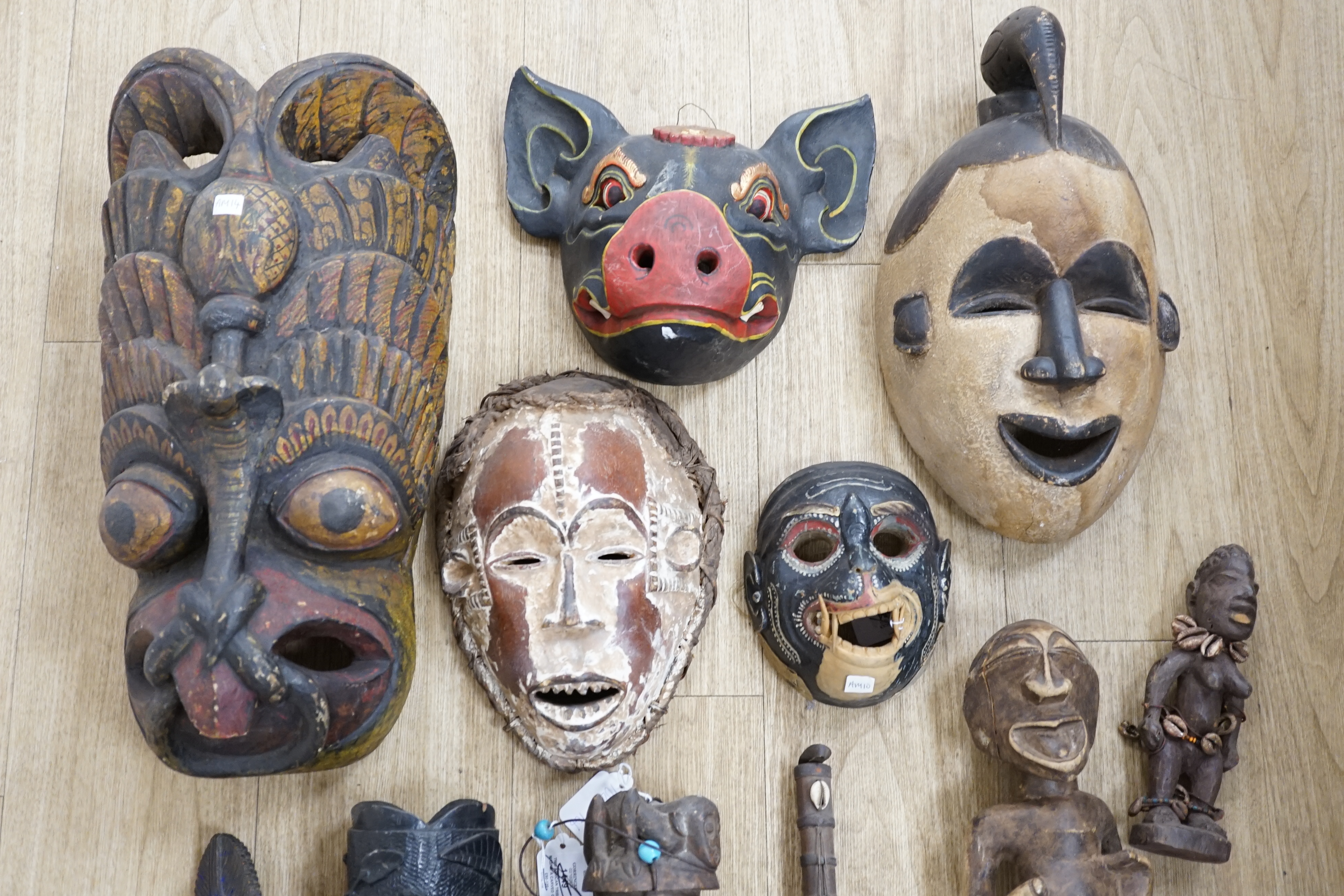 Eight Yoruba carved wood tribal figures, terracotta vessel, Ceylonese painted wood mask, East Java mask, pig mask, to African tribal masks, carved gourd vessel, four wood carvings and an instrument, largest 50cm